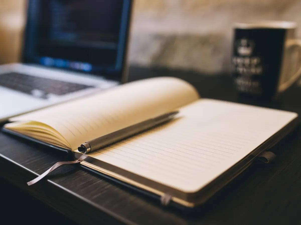 Open notitieboek met pen naast een laptop