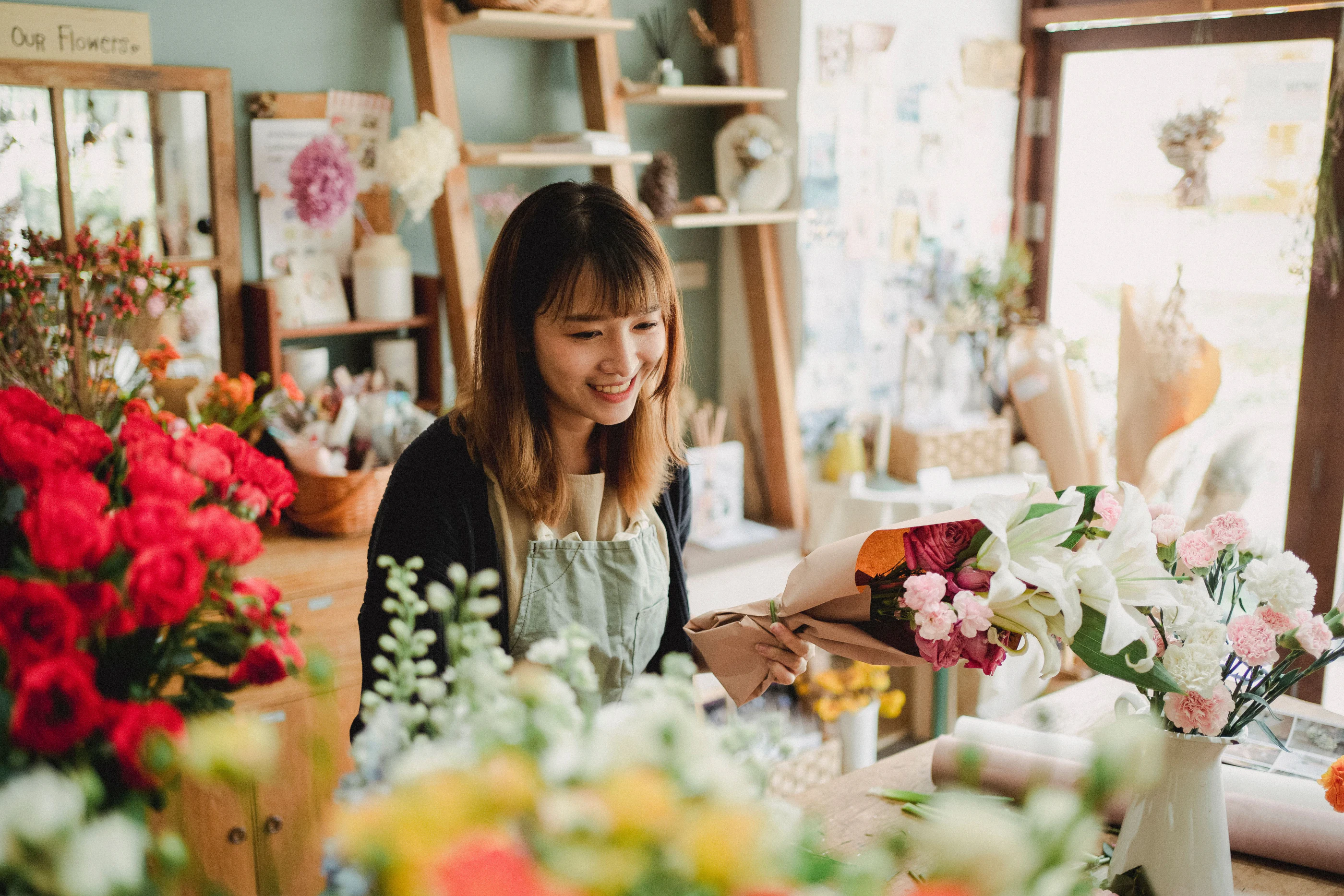Een bloemist lacht achter de toonbank van haar winkel vol bloemen