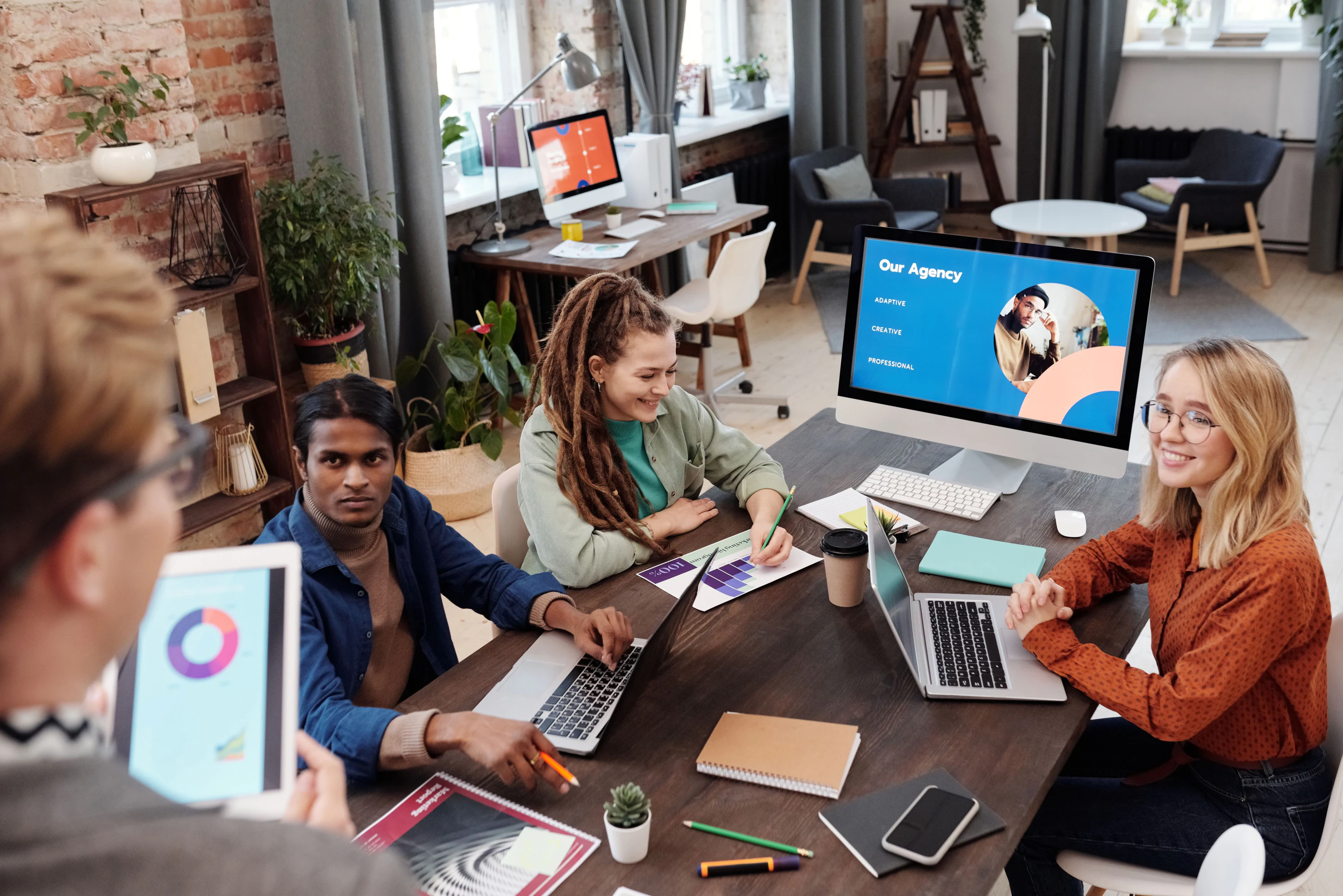 Een team van een webbureau overlegt rond een tafel met laptops en een groot scherm
