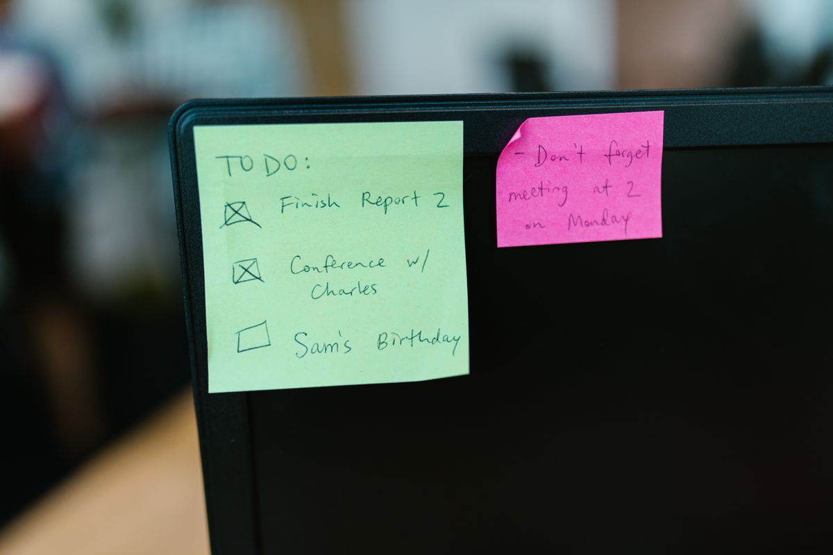 Gele en roze briefjes met notities geplakt op een computerscherm op een kantoorbureau